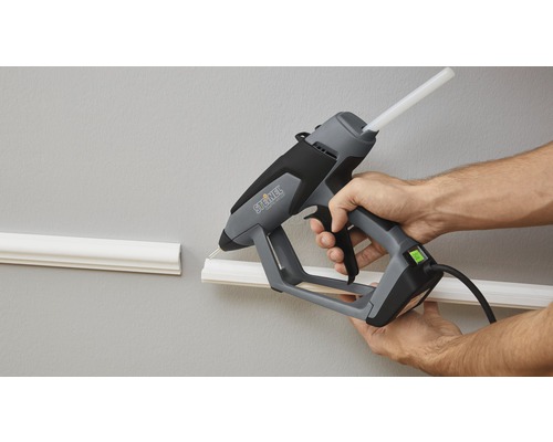 Une personne utilise un pistolet à colle Steinel pour fixer une moulure décorative sur un mur.