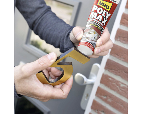 Une personne fixe un numéro de maison doré avec de la colle de montage.