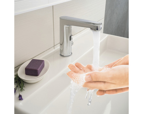 Person wäscht sich die Hände unter einem verchromten Wasserhahn im Badezimmerwaschbecken.