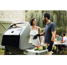 Un couple fait des grillades avec un barbecue à gaz dans le jardin. Des poivrons sont posés sur le grill.
