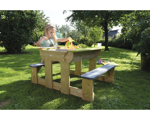 Enfant jouant à une table de pique-nique en bois avec fonction de bac à sable dans le jardin.