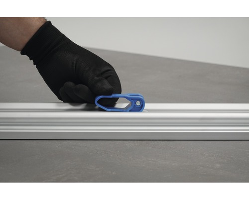 Eine Hand mit Schutzhandschuh befestigt einen blauen Schieber an einer Aluminiumschiene.