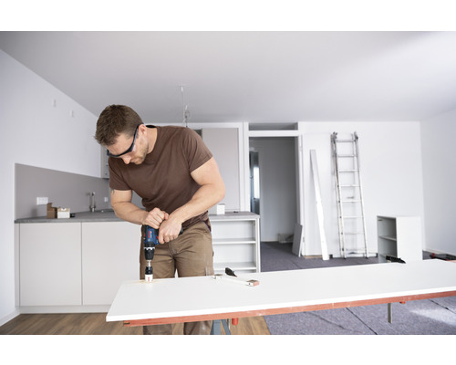 Un homme perce un trou dans un plan de travail avec une perceuse dans un appartement lumineux