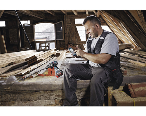 Mann mit Smartphone und Akku-Bohrschrauber im Dachgeschoss mit Holzbalken