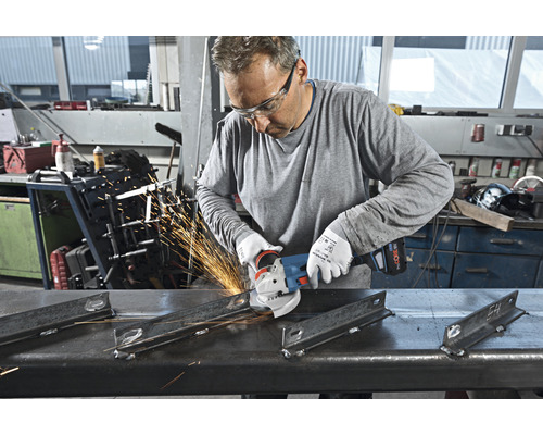 Ein Mann trägt eine Schutzbrille und benutzt einen Winkelschleifer, um Metall zu schleifen, wobei Funken entstehen.