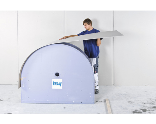 Un homme pose une plaque de plâtre avec le logo Knauf