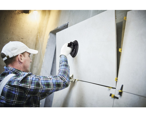 Fliesenleger mit Saugnapfwerkzeug verlegt Fliesen an einer Wand