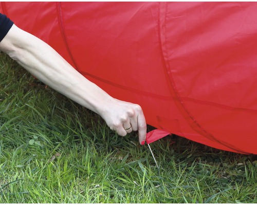 Detailaufnahme eines roten Spieltunnels, der mit Heringen im Gras befestigt wird