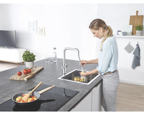 Frau wäscht Kartoffeln in einer Edelstahlspüle mit einem Chrom-Wasserhahn in einer Küche.