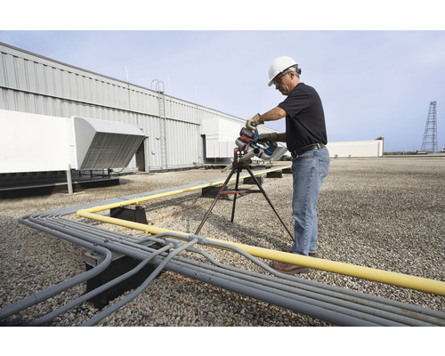 Un homme avec un casque de protection scie un tuyau sur un toit avec une scie à métaux.