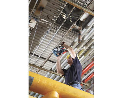 Un homme portant un casque de protection coupe un tuyau à l'aide d'une scie à tuyaux.