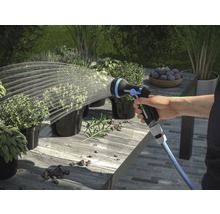 Hand bewässert Pflanzen mit einer Gartenspritze auf einem Tisch im Freien.