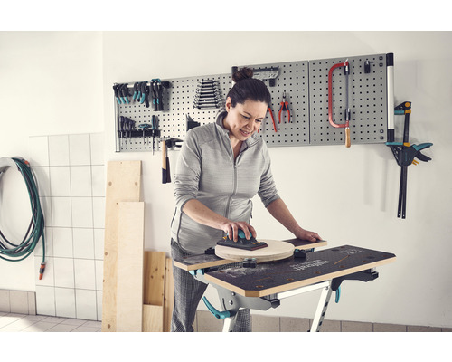Femme ponçant du bois sur un établi avec des outils sur un mur perforé