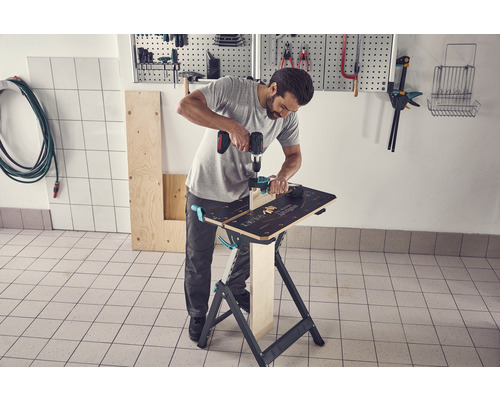 Un homme travaille avec une perceuse sur un établi dans un atelier.