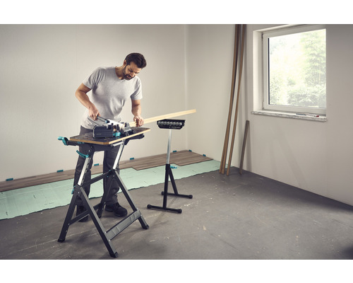 Un homme travaille avec une scie sauteuse sur un établi dans une pièce avec un sol stratifié.