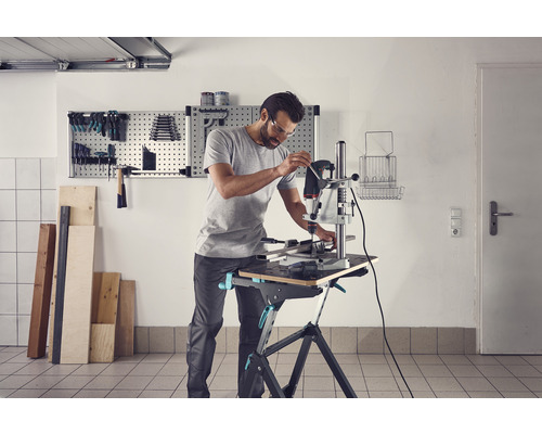 Un homme travaille avec une perceuse à colonne sur un établi dans un atelier.