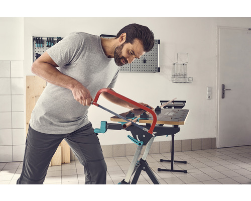 Un homme scie un tuyau sur un établi avec une scie à métaux.