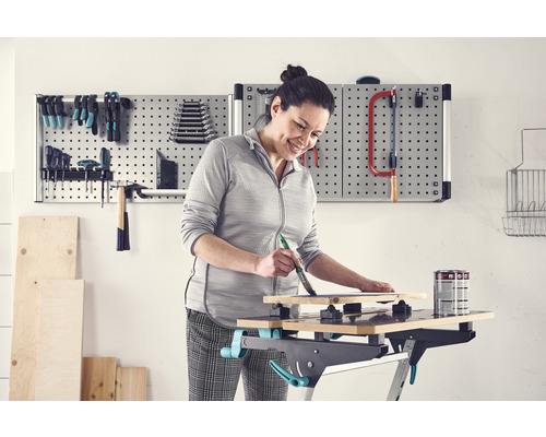 Femme peignant une planche de bois sur un établi dans un atelier avec un mur d''outils