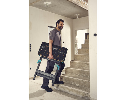 Un homme monte un établi pliant avec le logo Wolfcraft dans les escaliers