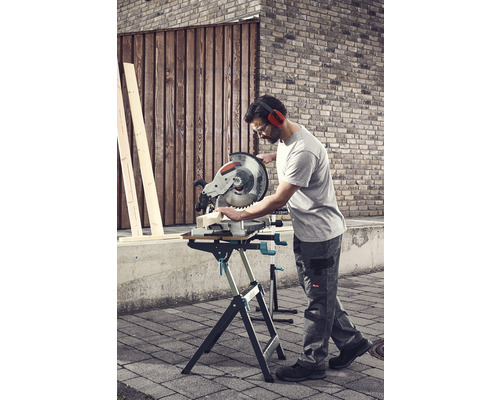 Un homme scie du bois avec une scie à onglet sur un établi à l''extérieur.