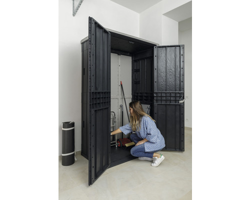 Offener Geräteschrank aus Kunststoff mit Lagergegenständen und einer Person, die sich davor befindet.