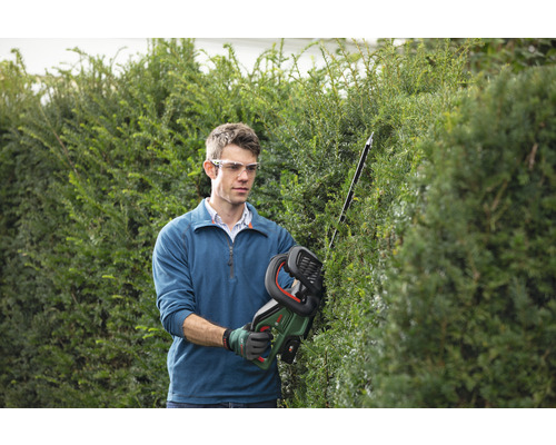 Mann schneidet Hecke mit Akku Heckenschere im Garten.