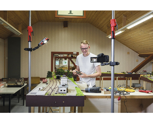 Un homme filme un train miniature avec une caméra sur un trépied et une lampe de travail.