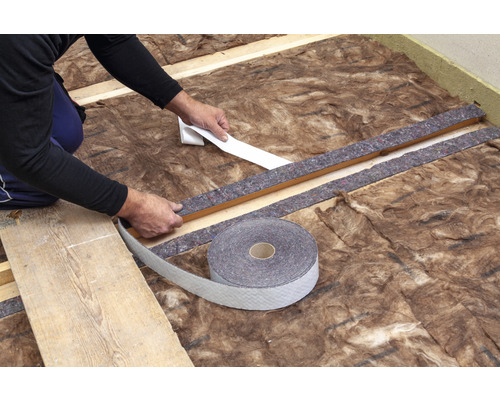 Artisan fixant une bande d''étanchéité sur de la laine isolante et un cadre en bois pour l''isolation