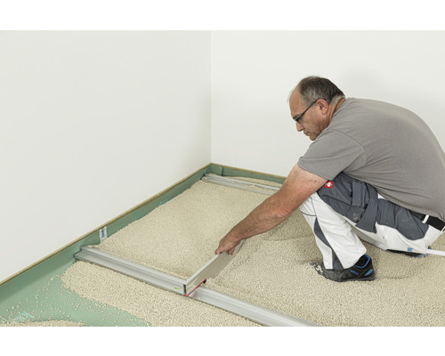 Mann nivelliert Trockenschüttung mit Nivellierschiene auf dem Boden