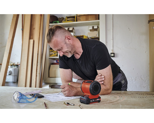 Un homme travaille sur un plan avec une lampe à batterie Einhell sur la table.