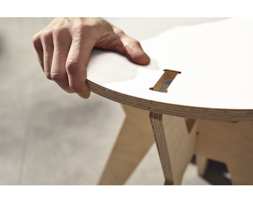 Nahaufnahme eines Hockers aus Schichtholz mit runder Sitzfläche, gehalten von einer Hand