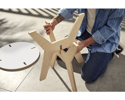 Person montiert einen Holztisch mit einer runden Tischplatte