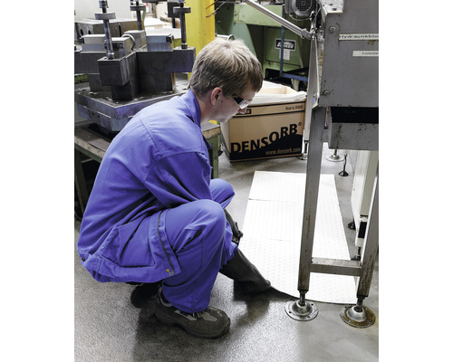 Un ouvrier en vêtements de travail pose des tapis absorbants dans une zone industrielle.