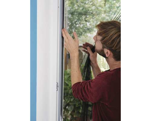 Mann montiert ein Fliegengitter an einem Fensterrahmen.