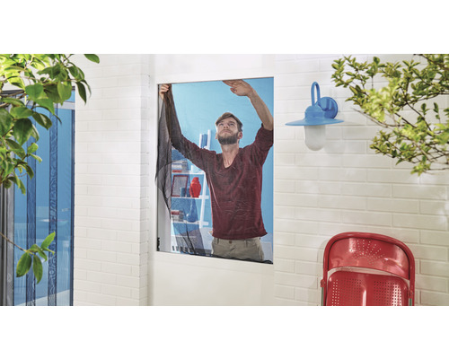 Un homme installe une moustiquaire sur une fenêtre.