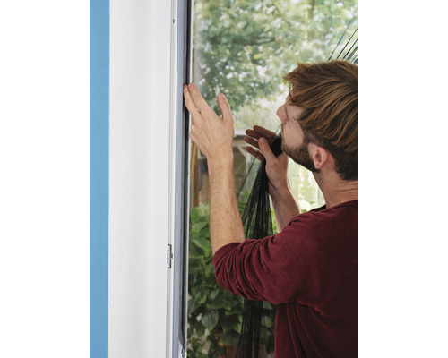 Mann befestigt ein Fliegengitter an einem Fensterrahmen.