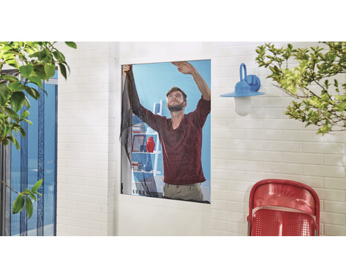 Un homme installe une moustiquaire sur une fenêtre.