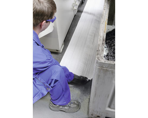 Une personne en vêtements de travail pose un tapis absorbant l''huile dans un atelier.