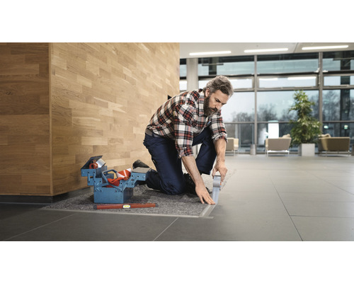 Handwerker verlegt Bodenschienen in einem Gebäude, Werkzeugkasten und Wasserwaage liegen bereit.