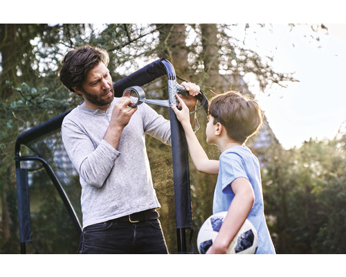 Vater und Sohn reparieren ein Fußballtor mit Klebeband im Garten.