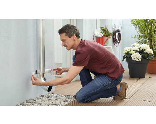 Un homme fixe une descente pluviale à un mur de maison avec du ruban d''étanchéité.