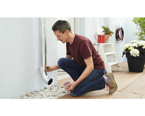 Un homme fixe un tuyau de descente sur un mur extérieur de maison.