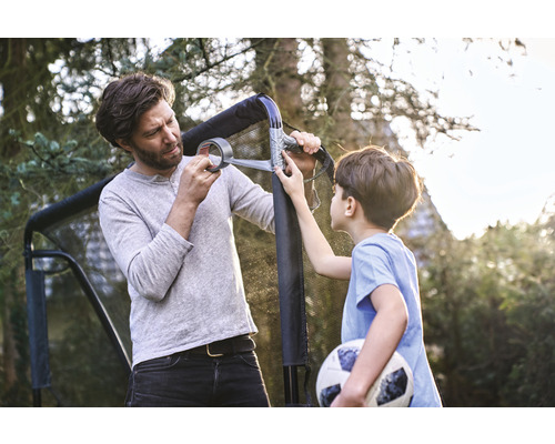 Père et fils réparent un but de foot avec du ruban adhésif dans le jardin.