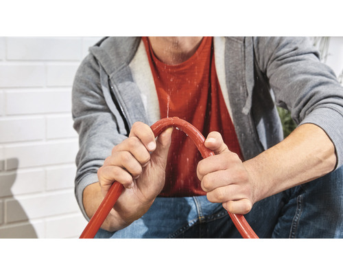 Une personne tient un tuyau d''arrosage qui fuit.