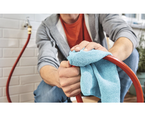 Un homme nettoie un tuyau d''arrosage avec un chiffon en microfibres.
