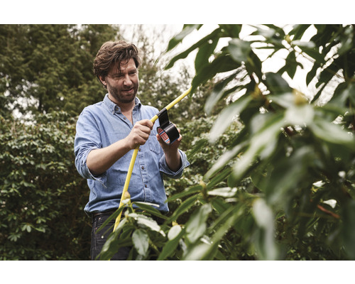 Un homme répare un tuyau d''arrosage jaune avec du ruban isolant dans le jardin.
