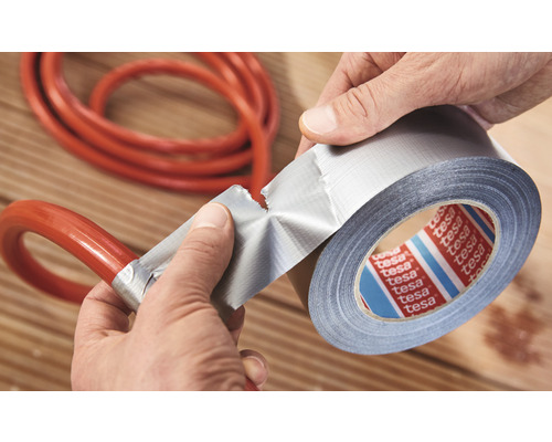 Une personne répare un tuyau avec du ruban adhésif toilé Tesa