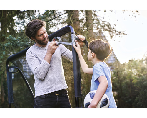 Un père et son fils réparent un but de foot avec du ruban adhésif dans le jardin.
