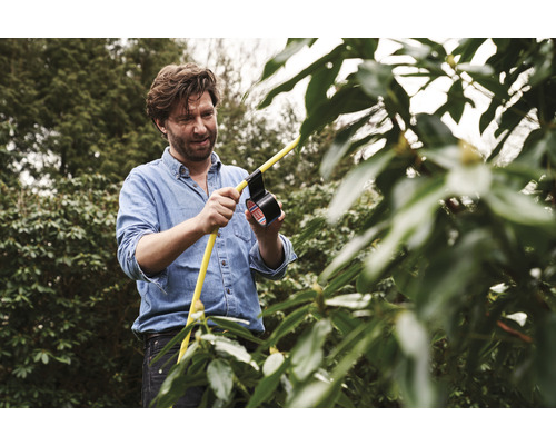 Un homme répare un tuyau d''arrosage jaune avec du ruban isolant dans le jardin.