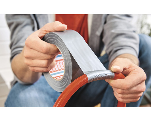 Une personne répare un tuyau d''arrosage avec du ruban adhésif toilé.